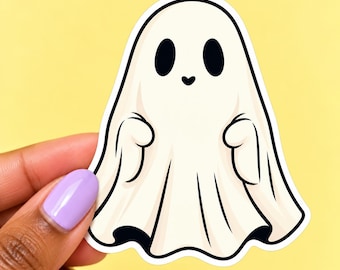 May include: A die-cut sticker featuring a cartoon ghost with a cream-colored body, two large oval black eyes, and a small black heart-shaped mouth. The ghost has a thick black outline and is depicted with two small arms raised at its sides.