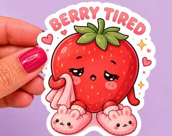 May include: A sticker featuring a cartoon strawberry with a sad expression, wearing bunny slippers and holding a tissue. The text "BERRY TIRED" is above the strawberry. The sticker has a white border and is held by a hand.