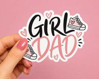 May include: A white sticker with the words "GIRL DAD" in black and pink, featuring two pink sneakers and heart illustrations. The sticker is held by a hand with pink nail polish against a pink background.