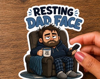 May include: A die-cut sticker featuring a cartoon illustration of a tired person with messy hair and a beard sitting in a brown armchair, holding a mug labeled DAD FUEL and a remote control, with the text RESTING DAD FACE in blue letters above.