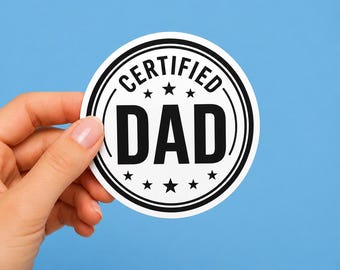 May include: A round, white sticker with a black border and the words "CERTIFIED DAD" in bold, black letters. The sticker has a blue background and is held by a hand.