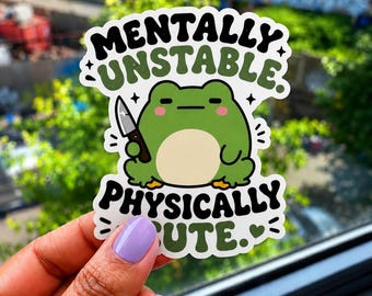 May include: A sticker with the text "MENTALLY UNSTABLE PHYSICALLY CUTE" in black and green. The sticker features a green frog holding a knife. The background is blurred, showing greenery and a cityscape.