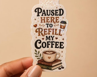 May include: A magnetic bookmark with a holographic finish featuring the text PAUSED HERE TO REFILL MY COFFEE. The design includes a coffee cup, a stack of two books, coffee beans, and a small leafy sprig in brown, green, and cream tones.
