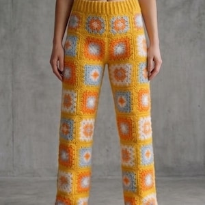 Puede incluir: Pantalones de crochet amarillos con un diseño de patchwork con cuadrados naranjas, blancos y azul claro. Los pantalones tienen cintura alta y pernera recta. El trabajo de crochet es detallado y los colores son vibrantes.