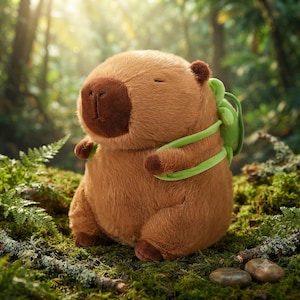 May include: A plush capybara toy with light brown fur, a dark brown snout, and closed eyes. The stuffed animal features a small green backpack with light green straps worn over its shoulders, giving it a rounded, soft appearance and texture.