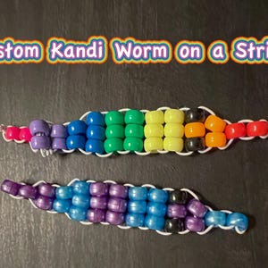 May include: Two beaded Kandi worms on a string, one in rainbow colors and the other in shades of purple and blue. The text "Custom Kandi Worm on a String" is above the worms in a rainbow font.
