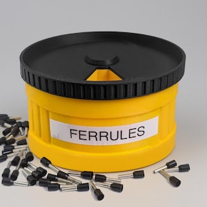 May include: A yellow container with a black lid and the word "FERRULES" on a white label. Several black and silver ferrules are scattered around the container. The container is cylindrical.