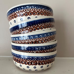May include: A stack of four ceramic bowls featuring a cream-coloured base with a hand-painted pattern of dark blue and brown circles. The design includes a wide band of speckled blue and a repeating motif of brown rings with blue centres.