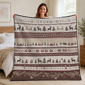 Könnte beinhalten: Eine gesteppte Wohndecke mit einem sich wiederholenden horizontalen Muster aus Rentieren, Tannenbäumen, kleinen Häusern, Schneeflocken und Herzformen in Creme-, Braun- und Dunkelrottönen, abgerundet durch einen dunklen Rand und Weihnachtsschmuck.