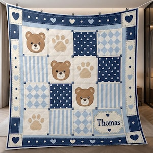 May include: A square patchwork quilt featuring a repeating pattern of brown teddy bear faces, beige paw prints, navy blue polka dots, and light blue diamonds and stripes. The quilt includes a white label with the name Thomas in navy blue text.