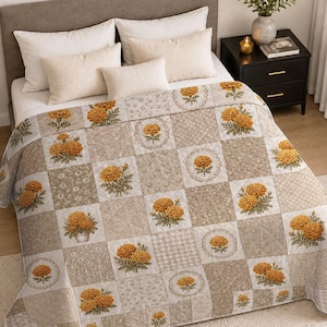 May include: A patchwork quilt featuring alternating squares of beige floral patterns, polka dots, and checkered prints. The quilt is decorated with repeating illustrations of orange marigold flowers, some contained within circular lace-like borders.