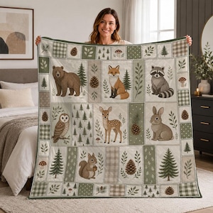 May include: A quilted throw blanket featuring a woodland theme with illustrations of a bear, fox, raccoon, owl, deer, rabbit, and squirrel. The design includes pine trees, pinecones, mushrooms, and plaid patterns in shades of green, brown, and cream.