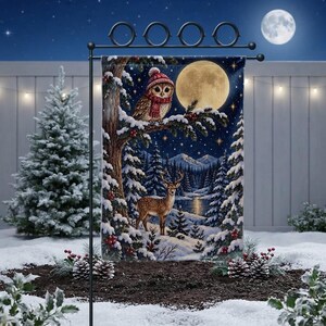 May include: A rectangular garden flag featuring a winter night scene with a full moon, a snowy forest, a deer standing in the snow, and an owl wearing a red knit hat and scarf perched on a tree branch, all suspended from a black metal stand.
