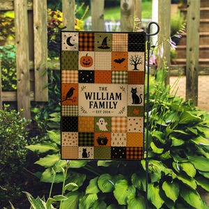 May include: A rectangular garden flag featuring a patchwork design of orange, black, green, and cream squares with Halloween motifs including a pumpkin, witch hat, bat, ghost, cat, and tree. The center text reads THE WILLIAM FAMILY EST 2014.