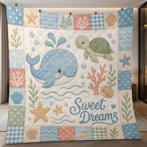 May include: A quilted blanket featuring a blue whale, a green sea turtle, coral, seashells, and starfish on a cream background. The border consists of patterned squares in blue, green, and peach. The text "Sweet Dreams" is printed in blue script.
