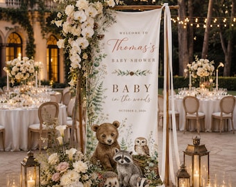 Peut inclure: Une bannière verticale en tissu avec le texte "WELCOME TO Thomas's BABY SHOWER BABY in the woods OCTOBER 2, 2026" et des illustrations d'un ourson, d'un raton laveur, d'un hibou, d'un hérisson et d'un blaireau, ornée de fleurs blanches et de lanternes.