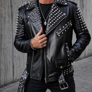 May include: A black leather motorcycle jacket featuring silver-toned metal spikes on the shoulders and lapels. The jacket includes a front zip closure, zipped pockets, a buckled belt at the waist, and silver stud embellishments along the hem.