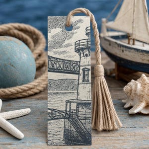 May include: A rectangular bookmark made of off-white paper featuring a black ink illustration of a lighthouse and a bridge. The bookmark has a circular hole at the top with a thick, braided tan jute cord tied into a decorative tassel.