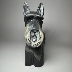 May include: A black and white dog figurine with pointed ears and a textured muzzle. The sculpture features a dark body with lighter highlights around the face and snout, capturing the distinct facial features of a terrier breed in a standing pose.