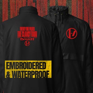 May include: A black windbreaker jacket featuring a high collar and front zip. The back displays red text reading "TWENTY ONE PILOTS THE CLANCY TOUR BREACH" above a red circular logo. A yellow rectangular graphic reads "EMBROIDERED & WATERPROOF".