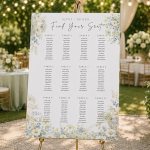 May include: A white wedding seating chart sign on a gold easel featuring the text Olivia and Michael Find Your Seat, organized into twelve tables with guest names, decorated with blue and white floral illustrations at the top and bottom corners.