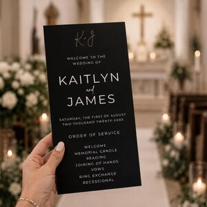 Può includere: Un cartoncino rettangolare nero per il programma del matrimonio con testo bianco che recita Welcome to the wedding of Kaitlyn and James, Saturday, the first of August two thousand twenty-xxxx, Order of Service, Welcome, Memorial Candle, Reading, Joining of Hands, Vows, Ring Exchange, Recessional.