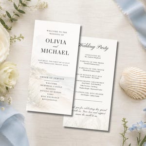 May include: Two white wedding program cards with black serif text. The front card displays "Welcome to the wedding of Olivia and Michael" and an order of service. The back card lists the wedding party members and a thank you message.