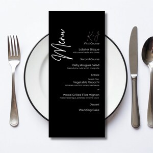 Może przedstawiać: Czarna prostokątna karta menu z białym tekstem zawierającym słowo Menu, K+J oraz listę dań, w tym Lobster Bisque, Baby Arugula Salad, Vegetable Gnocchi, Wood-Grilled Filet Mignon i Wedding Cake, umieszczona na białym talerzu.