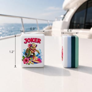 Pode incluir: Duas pe&ccedil;as retangulares brancas de mahjong com um gr&aacute;fico de uma tartaruga marinha verde usando &oacute;culos de sol e um colar de flores enquanto surfa numa prancha colorida. O texto JOKER est&aacute; impresso a vermelho. Dimens&otilde;es: 3,05 cm por 2,29 cm por 1,52 cm.