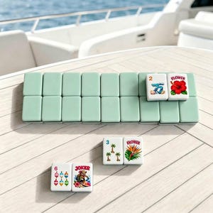 Pode incluir: Um conjunto de pe&ccedil;as retangulares de mahjong com verso verde-claro e frente branca. Algumas pe&ccedil;as apresentam ilustra&ccedil;&otilde;es coloridas de um hibisco vermelho, uma onda azul, palmeiras, uma flor ave-do-para&iacute;so, boias de pesca e uma tartaruga surfista.