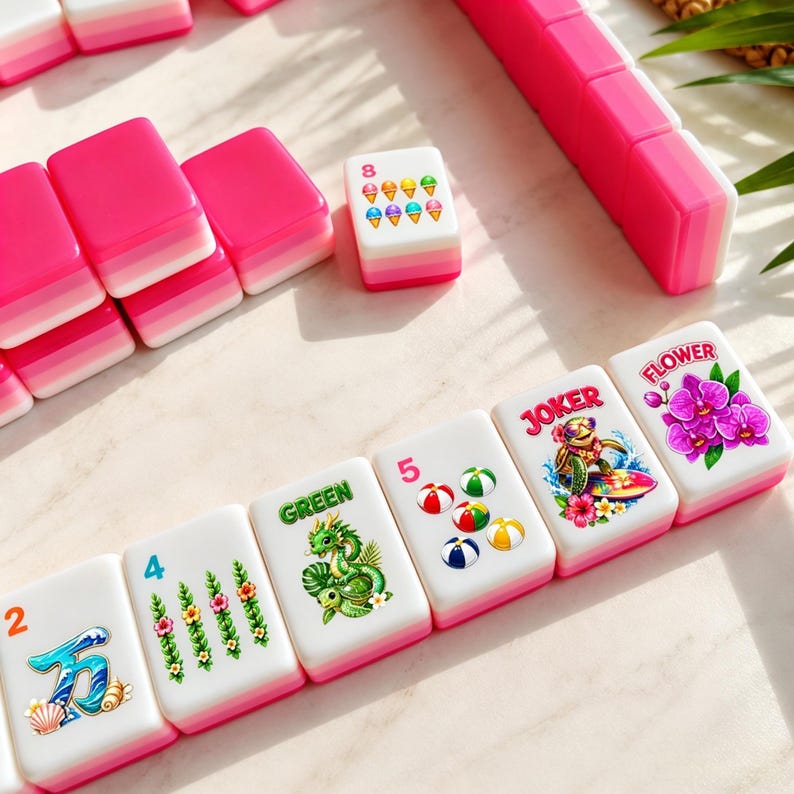 May include: A set of pink and white Mahjong tiles with various colorful illustrations and numbers. The tiles feature images of flowers, dragons, and ice cream cones. The set includes a pink tile holder.