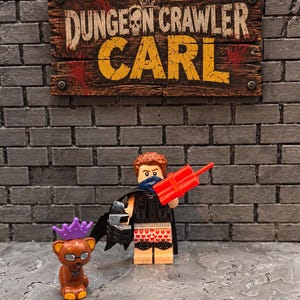 May include: A Lego minifigure with brown hair, a blue bandana, a black vest, and heart-patterned boxers, holding red dynamite. Beside it stands a brown cat figure wearing a purple crown and glasses, beneath a sign reading Dungeon Crawler Carl.