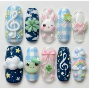 May include: A set of ten press-on nails featuring 3D designs including a white treble clef, a green four-leaf clover, a winking white rabbit, a shooting star, a winged heart, a white cloud, a green frog, a pink bow, and a colorful rainbow.