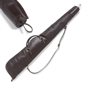 Puede incluir: Una funda para arma de cuero marrón oscuro con acabado texturizado, un asa de transporte resistente y una correa ajustable para el hombro. La funda incluye herrajes de metal color latón y un lazo en el extremo, con una vista detallada de la tapa.