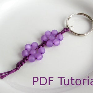 May include: A purple beaded keychain with a silver key ring. The beads are arranged in a flower shape. The keychain has a purple cord with a tassel. The image includes the text "PDF Tutorial".