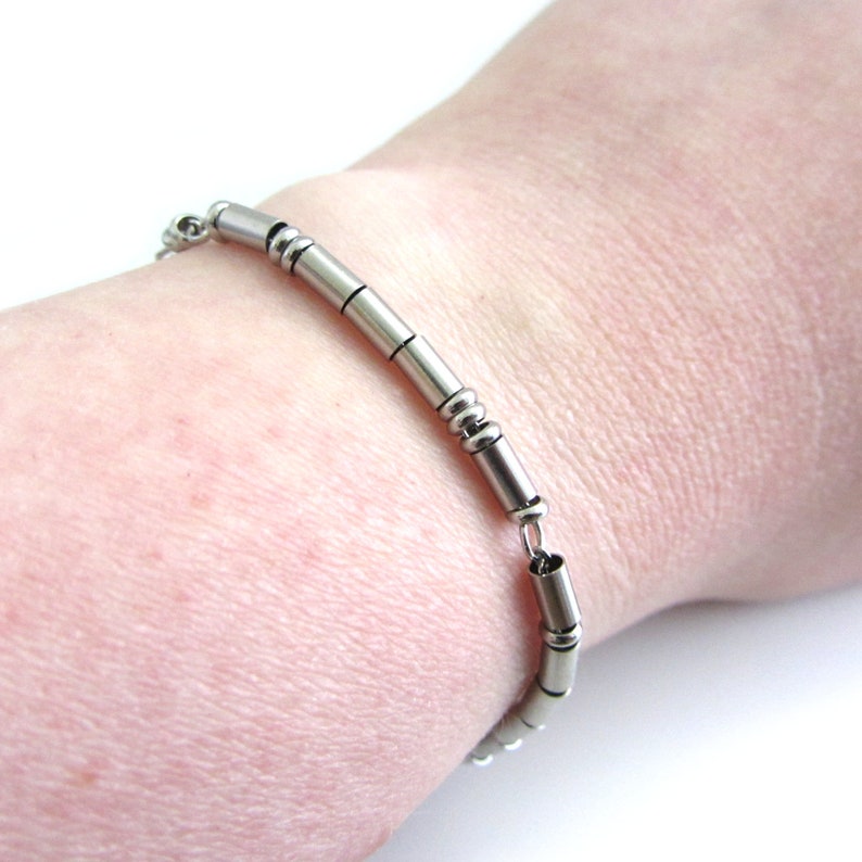 A stainless steel I love you Morse Code bracelet (thin round and cylinder beads spell out the message) with a fine cable chain. Shown worn on wrist for wearer to read.