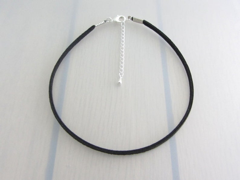 Puede incluir: Un collar gargantilla negro con un cierre y una cadena extensora plateados. El collar est&aacute; hecho de un material fino, redondo, similar al ante. El cierre y la cadena son visibles en la parte posterior del collar.