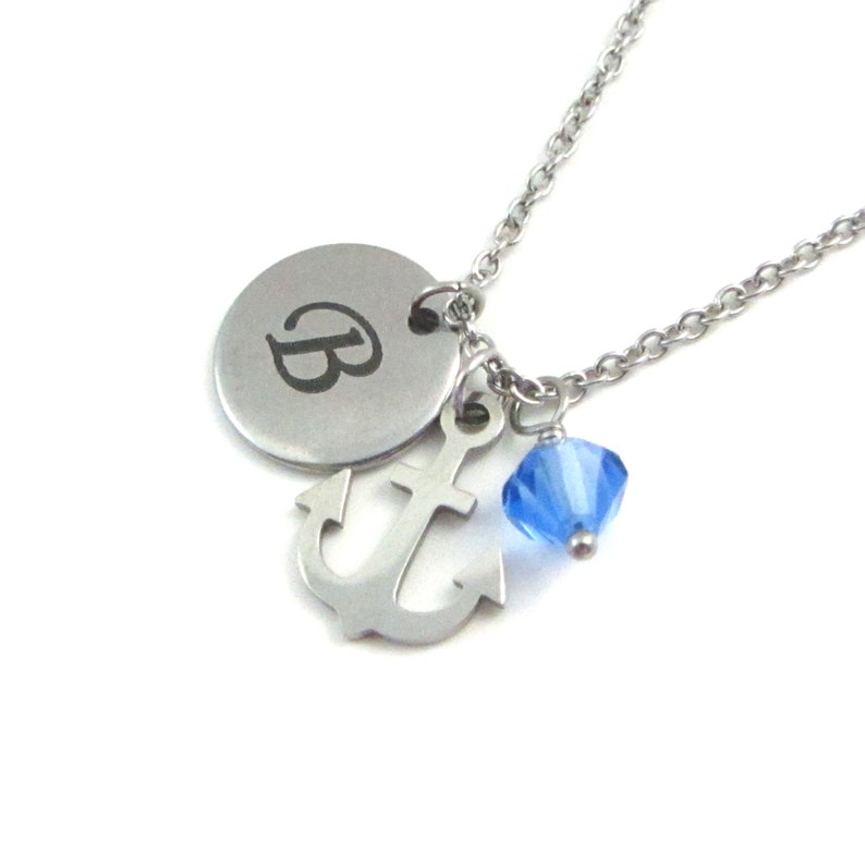 Engraved letter B on a round stainless steel disc charm, with an anchor charm and a blue bicone crystal charm all on a thin stainless steel chain to create a necklace.