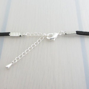Puede incluir: Primer plano de un collar de cord&oacute;n negro con una cadena y un cierre de color plateado. La cadena ajustable se extiende desde el cord&oacute;n principal, lo que permite un ajuste personalizado. El collar se muestra sobre un fondo claro.
