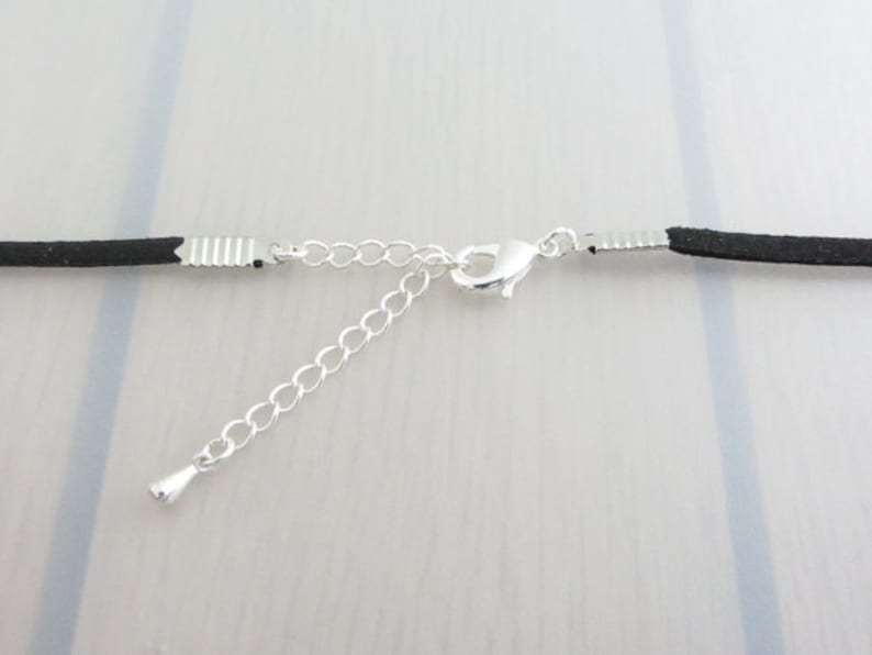 Puede incluir: Primer plano de un collar de cord&oacute;n negro con una cadena y un cierre de color plateado. La cadena ajustable se extiende desde el cord&oacute;n principal, lo que permite un ajuste personalizado. El collar se muestra sobre un fondo claro.