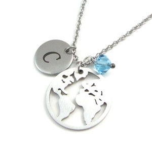 May include: A silver necklace with a charm of a world map, a small blue crystal, and a round charm with the letter C engraved on it.