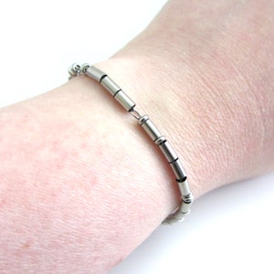 A stainless steel I am enough Morse Code bracelet (thin round and cylinder beads spell out the message) with a fine cable chain. Shown worn on wrist for wearer to read.