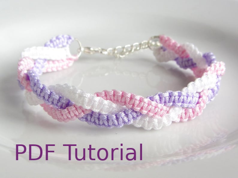 A bracelet that has a 3 braid effect. Each braid is made using square knots and each braid is in a separate colour - white, lilac and pink. With a metal chain and clasp closure. With PDF Tutorial written on the image.