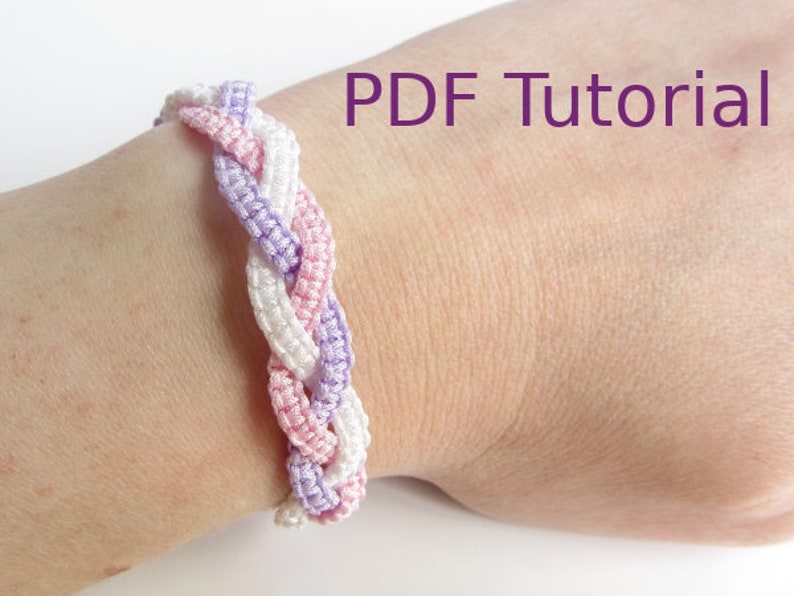 A bracelet that has a 3 braid effect shown worn on wrist. Each braid is made using square knots and each braid is in a separate colour - white, lilac and pink. With a metal chain and clasp closure. With PDF Tutorial written on the image.