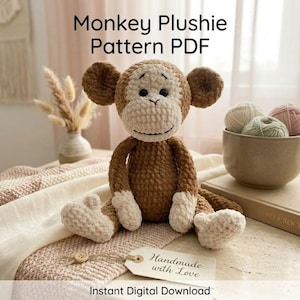May include: A crocheted monkey plushie with brown and cream-colored yarn, sitting on a patterned blanket. The image includes text that reads "Monkey Plushie Pattern PDF" and "Handmade with Love". A bowl of yarn balls is also visible.