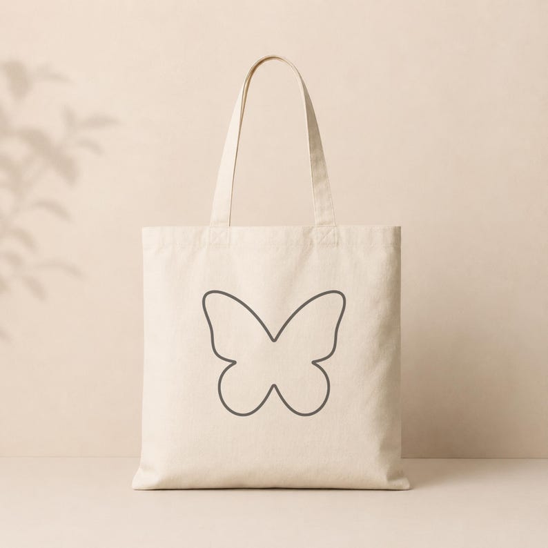 Peut inclure: Sac fourre-tout cr&egrave;me avec un motif de contour de papillon gris fonc&eacute;. Le sac est de forme rectangulaire avec une poign&eacute;e pour le transport. Le motif de papillon est centr&eacute; sur le devant du sac.