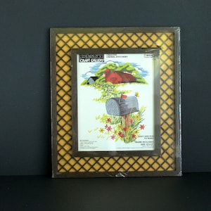 May include: Framed embroidery kit featuring a rural scene with a red barn, mailbox, and flowers. The frame has a dark wood finish with a yellow diamond pattern. The kit includes the text "The Craft Gallery".