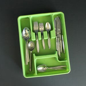 Może przedstawiać: Zielona plastikowa taca na sztućce wypełniona srebrnymi sztućcami. Sztućce obejmują łyżki, widelce i noże. Taca jest prostokątna z wieloma przegródkami do organizacji przyborów. Sztućce są wykonane z błyszczącego, srebrnego metalu.