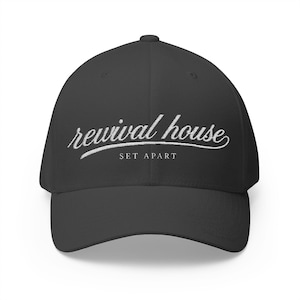 Peut inclure: Une casquette de baseball noire avec une inscription brodée en blanc sur le devant. Le texte indique "revival house" dans une police cursive, avec les mots "SET APART" en lettres capitales plus petites juste en dessous.