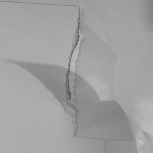 May include: A white sheet of paper with a vertical tear running down the center. The paper is partially separated, with the torn edges showing a rough, fibrous texture. The lighting creates a shadow along the jagged split, highlighting the depth.